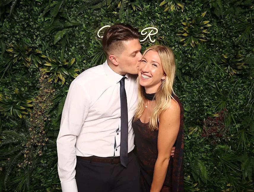 Couple photographié au photobooth devant le mur végétal avec enseigne au néon